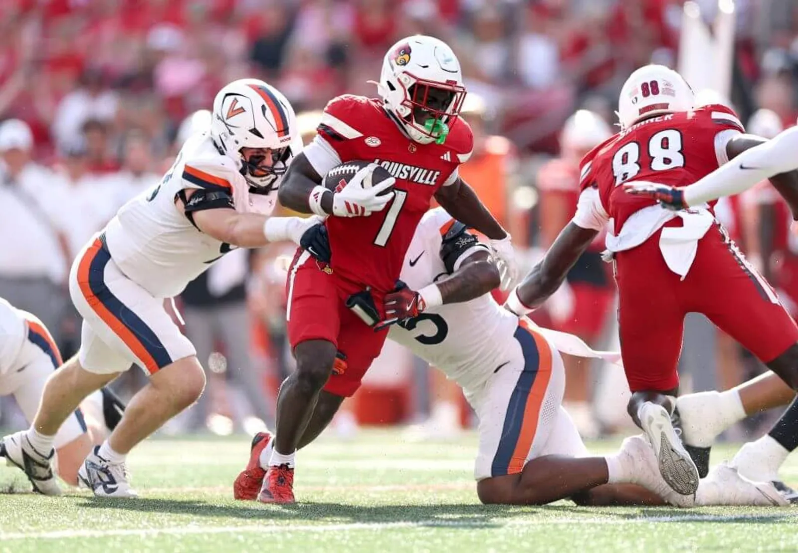 Louisville's Isaac Brown runs with the football while being tackled by two Virginia players