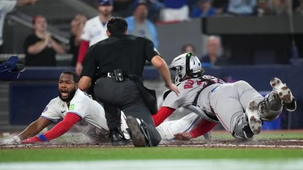 Toronto Blue Jays first baseman Vladimir Guerrero Jr. , left, scores a run past Boston Red Sox catcher Adley Rutschman during the eighth inning Wednesday night. (Nathan Denette/The Canadian Press via AP)