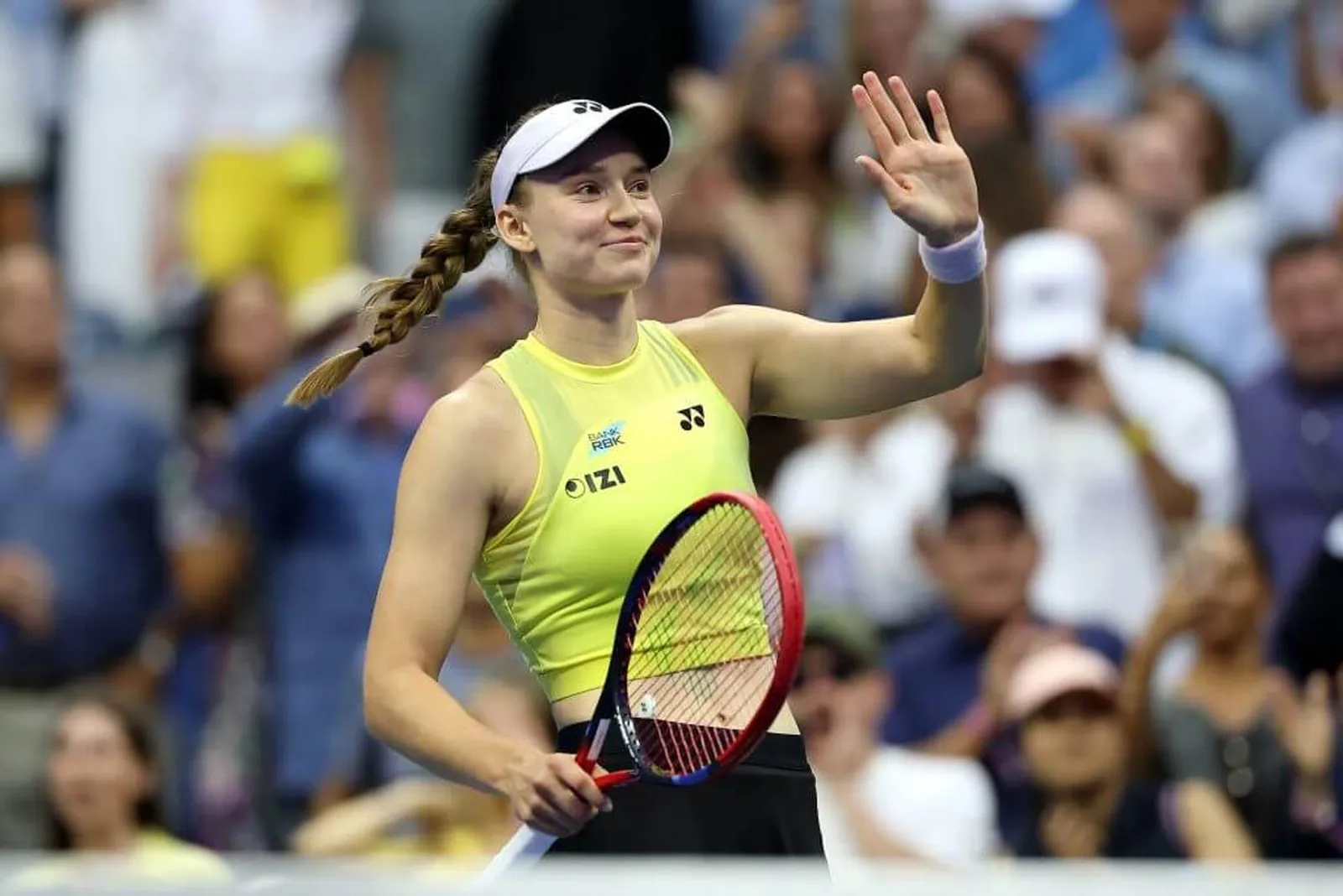 Elena Rybakina waves with a smile on a tennis court.